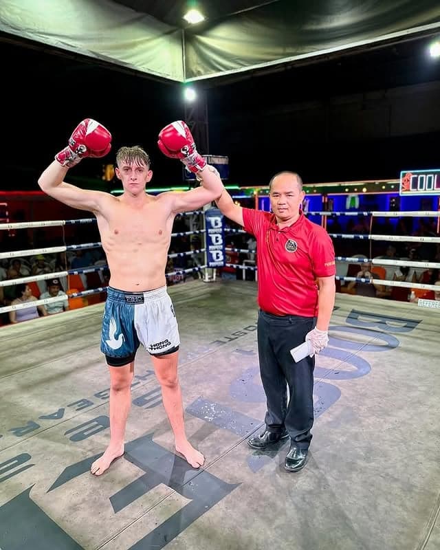 Zac in the ring with both gloves raised after his first professional Muay Thai fight