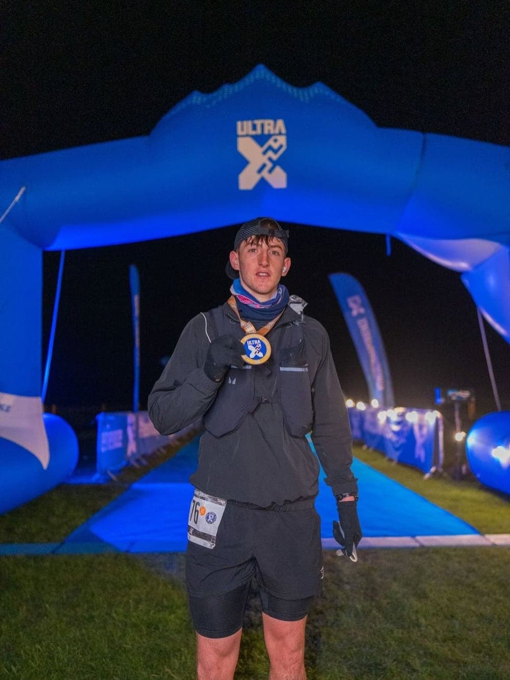 Zac at the Ultra X finish arch at night, holding his medal